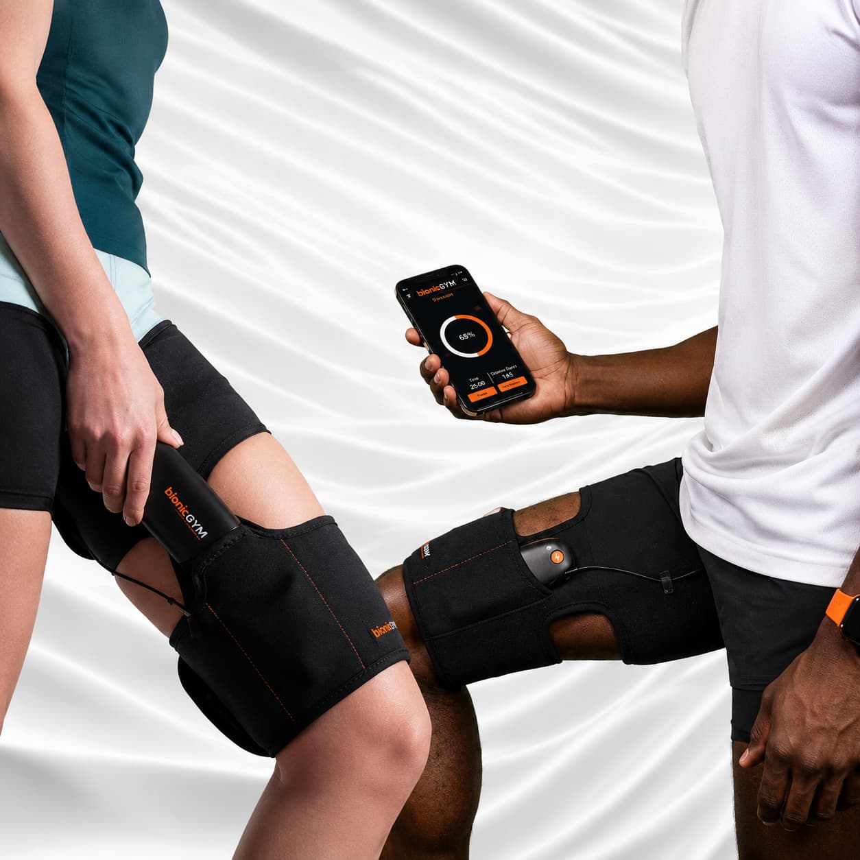 Two people wearing BionicGym muscle stimulator devices, with one holding a smartphone displaying the companion app, set against a white draped fabric background.